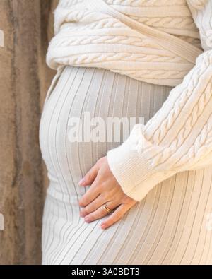 Donna incinta in un abito a maglia di colore chiaro che tiene la pancia. Senza faccia. Gravidanza sana e felice, in attesa del bambino. Foto Stock