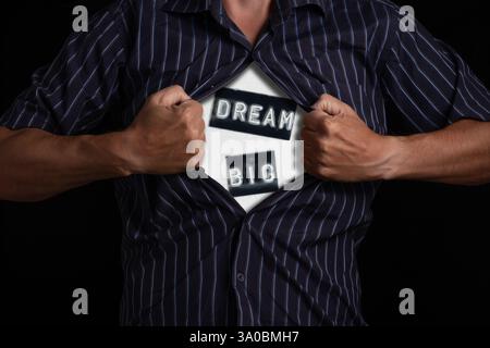 Uomo che si lacera aprendo la camicia per mostrare la parola, Dream Big, isolato su sfondo nero. Dimostrazione di motivazione e aspirazione Foto Stock