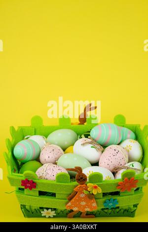 Uova di Pasqua colorate in un cestino verde su sfondo giallo. Festa di Pasqua. Foto di alta qualità Foto Stock