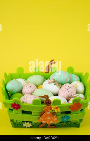 Uova di Pasqua colorate in un cestino verde su sfondo giallo. Festa di Pasqua. Foto di alta qualità Foto Stock