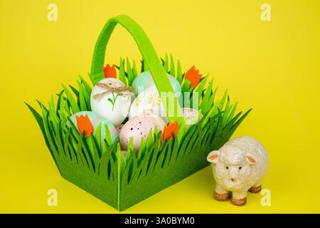 Cestino verde con uova di Pasqua colorate e pecore su sfondo giallo. Foto di alta qualità Foto Stock