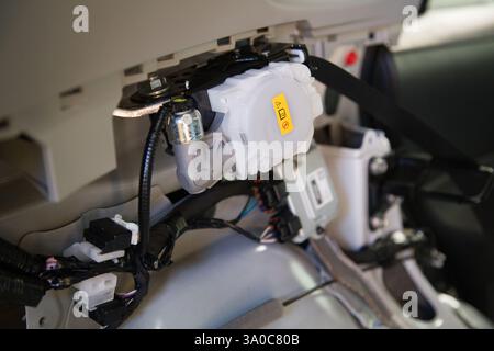 Vista dell'abitacolo di una vettura senza elementi decorativi, dell'unità riavvolgitore cintura di sicurezza passeggero posteriore di una vettura, del cablaggio e di altri moduli relativi alla sicurezza Foto Stock