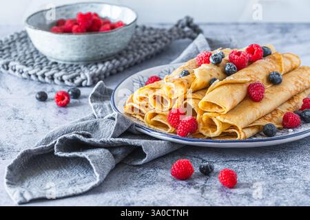 Piatto con pila di pancake arrotolati con lamponi e mirtilli su sfondo azzurro Foto Stock