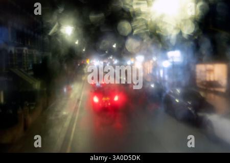 Vista sfocata dei colorati semafori posteriori rossi nel traffico di strada di notte attraverso un autobus a due piani Raininy Window Londra Regno Unito Foto Stock