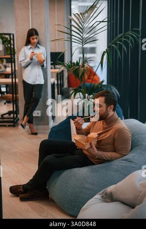 Gli impiegati si trovano nella zona di riposo e stanno facendo una pausa e mangiando cibo da scatole ecologiche di carta. Foto Stock