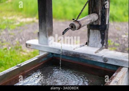 Primo piano di una vecchia pompa di legno con acqua che scorre in una vaschetta. Il fascino rustico di questa pompa vintage evoca nostalgia per tempi più semplici e tradizionali Foto Stock