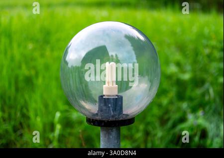 Luce per esterni con ampie sfere di vetro che ospitano lampadine fluorescenti, che illuminano l'ambiente circostante. Sullo sfondo si estende un prato verde lussureggiante Foto Stock