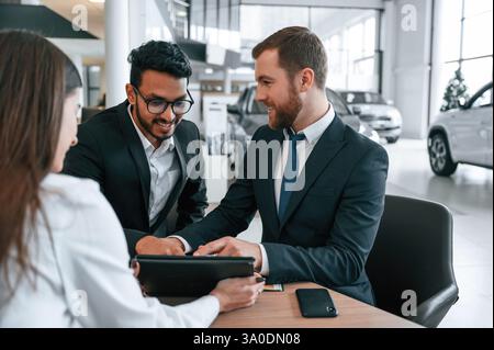 Due uomini comprano un'automobile. Tre persone lavorano insieme nello showroom dell'auto. Foto Stock