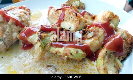 Le lancette di zucchine grigliate riposano invitantemente su un piatto bianco pulito, ricoperto da vivace ketchup rosso, che mostra una deliziosa creazione culinaria perfetta per Foto Stock