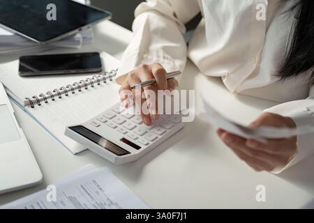 Calcolo dei dati finanziari con una calcolatrice durante la revisione di ricevute e note per la preparazione fiscale. Foto Stock
