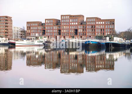 Moderni edifici residenziali e barche ormeggiate con riflessi sulle acque calme di Ijburg, Amsterdam Foto Stock