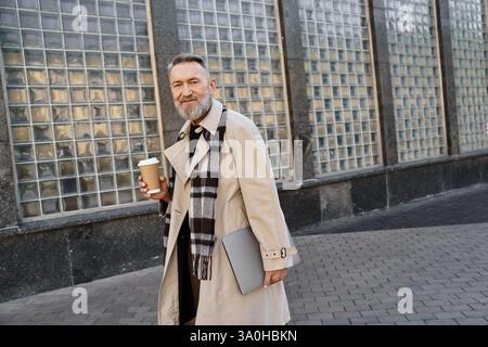 Un anziano cammina con sicurezza in un ambiente urbano, sorseggiando un caffè da una tazza usa e getta. Foto Stock
