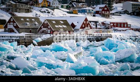 Una vista pittoresca di case colorate lungo una costa innevata, con grandi blocchi di ghiaccio che galleggiano nell'acqua. La scena cattura la bellezza dell'inverno Foto Stock
