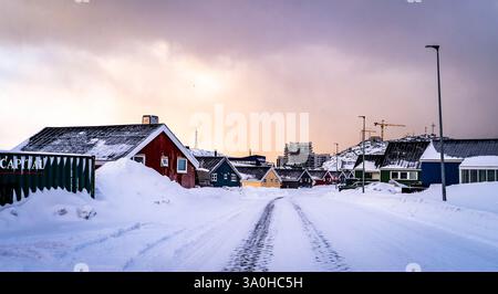 Una strada innevata fiancheggiata da case colorate in un paesaggio invernale. La scena cattura un'atmosfera serena con tetti innevati e un cielo nuvoloso, S. Foto Stock