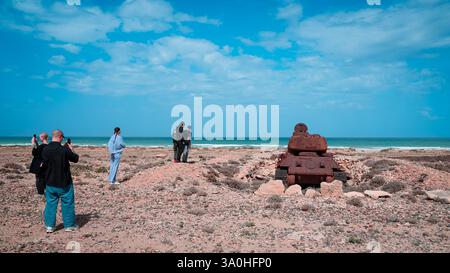 I turisti si meravigliano davanti a una reliquia arrugginita vicino alla spiaggia mentre si godono le splendide vedute costiere sull'isola di Socotra. Foto Stock