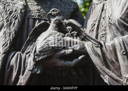 Una dettagliata scultura in bronzo a due mani che reggono dolcemente un paio di colombe, simboleggiando la pace e l'unità in una giornata nuvolosa Foto Stock