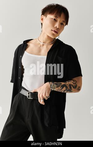 Il giovane uomo in prima linea posa con sicurezza in un abbigliamento elegante con intricati tatuaggi in mostra Foto Stock