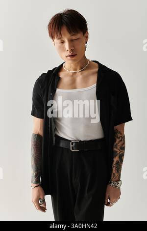 Un giovane uomo alla moda sfoggia uno stile unico con tatuaggi e abiti alla moda in un ambiente moderno. Foto Stock