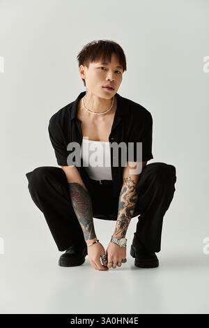 Un giovane uomo asiatico alla moda mette in mostra il suo stile accovacciandosi mentre trasuda fiducia e fascino. Foto Stock