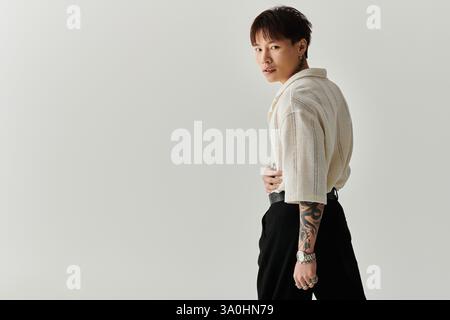 Giovane uomo asiatico alla moda mette in mostra il suo stile in un ambiente minimalista, trasudando fiducia. Foto Stock