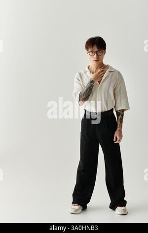 Giovane uomo alla moda mette in mostra il suo stile con fiducia in un ambiente moderno e neutrale. Foto Stock