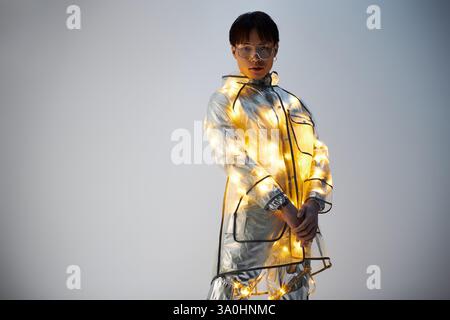 Un giovane ed elegante uomo asiatico mostra il suo cappotto scintillante, che irradia fiducia. Foto Stock