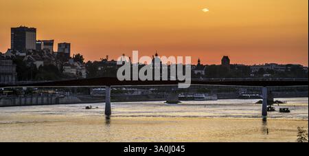 Un tranquillo tramonto su un fiume con un ponte moderno e lo skyline della città sullo sfondo. Foto Stock