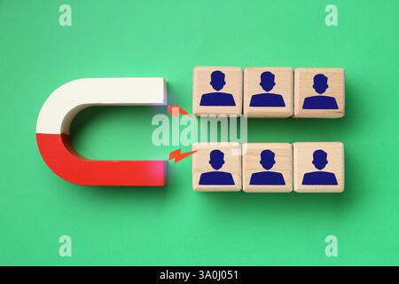 Magnete che attrae cubi di legno con figure umane su sfondo verde, vista dall'alto. Reclutamento o acquisizione di clienti Foto Stock