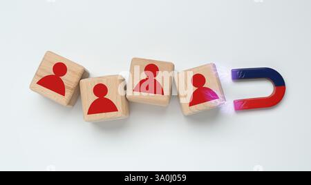 Magnete che attrae cubi di legno con figure umane su sfondo bianco, vista dall'alto. Reclutamento o acquisizione di clienti Foto Stock