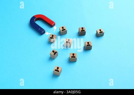 Magnete che attrae cubi di legno con figure umane su sfondo azzurro. Reclutamento o acquisizione di clienti Foto Stock