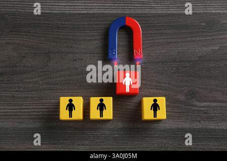Magnete che attrae uno dei cubi con figure umane su sfondo in legno, vista dall'alto. Reclutamento o acquisizione di clienti Foto Stock