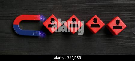 Magnete che attrae cubetti rossi con figure umane su sfondo in legno nero, vista dall'alto. Reclutamento o acquisizione di clienti Foto Stock