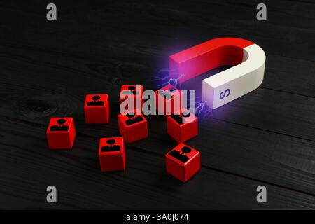 Magnete che attrae cubetti rossi con figure umane sul retro su sfondo in legno. Reclutamento o acquisizione di clienti Foto Stock