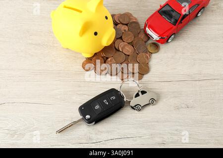 Chiave, modello, monete e salvadanaio su tavolo in legno chiaro, vista dall'alto. Comprare auto Foto Stock