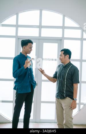 Due uomini, forse colleghi o amici, sono impegnati in una conversazione vivace all'interno di uno spazio luminoso e moderno. Stanno gestendo e sembrano essere discu Foto Stock
