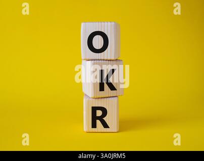 Obiettivi OKR e simbolo dei risultati chiave. Cubi in legno con parole obiettivi OKR e risultati chiave. Bellissimo sfondo giallo. Business e OKR. Foto Stock