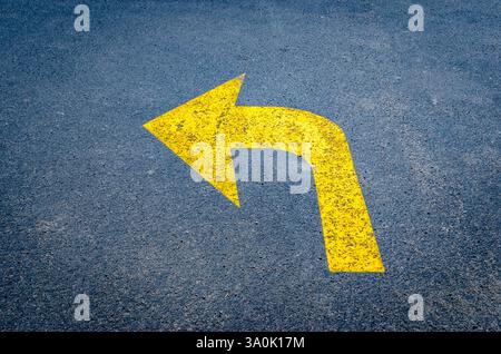 Freccia gialla sulla pavimentazione nera rivolta verso sinistra Foto Stock