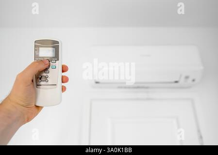 Mano di un uomo che dirige il telecomando verso il condizionatore d'aria. Foto Stock