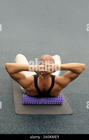 Punto di attivazione del massaggio schiena dell'atleta irriconoscibile con rullo in schiuma viola. Uomo caucasico adulto che fa esercizio di yoga. Verticale. Rilascio miofasciale. Cl Foto Stock