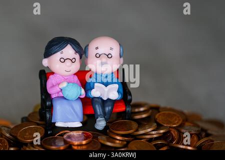 Simbolo di una pensione finanziariamente sicura, un paio di statuette di bambola seduto su un mucchio di monete Foto Stock