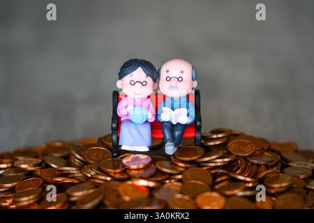 Simbolo di una pensione finanziariamente sicura, un paio di statuette di bambola seduto su un mucchio di monete Foto Stock