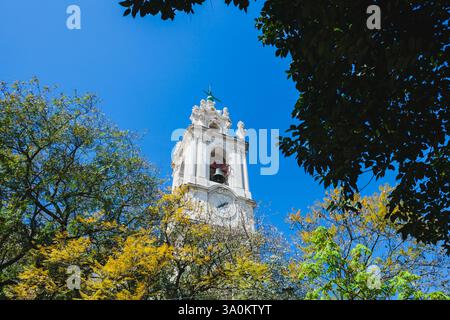 un'alta ed elegante torre bianca dell'orologio con intricati dettagli architettonici, probabilmente parte di una chiesa o di un edificio storico. La campana all'interno della torre è V Foto Stock