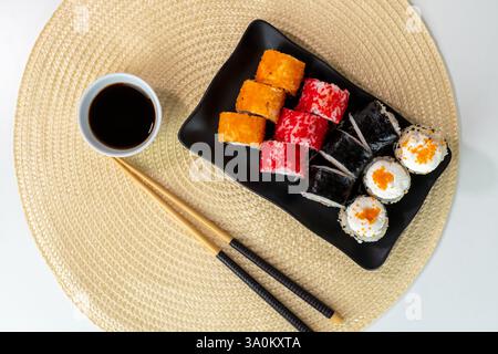 Sushi roll assortiti con salsa di soia su piatto nero e tappetino in tessuto Foto Stock