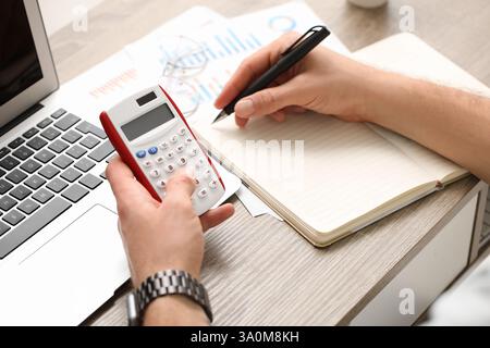 Mani maschili che scrivono qualcosa e fanno calcoli in ufficio. Primo piano Foto Stock