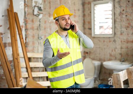 Giovane ingegnere civile bearded che parla al telefono in cantiere Foto Stock