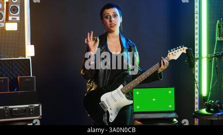 La rock star ribelle e cool esegue un'esibizione dal vivo accanto ai tasti Chroma del nightclub, sentendosi potente nella sua giacca in pelle e nel trucco scuro. Cantante potente e alla moda che si esibisce. Telecamera A.. Foto Stock