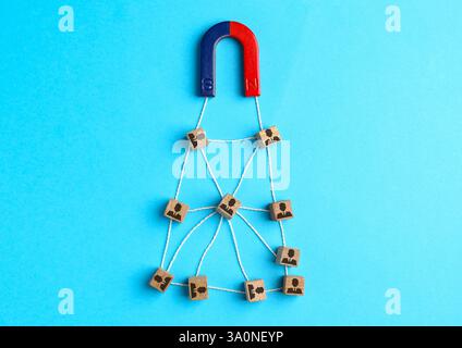 Magnete che attrae cubi di legno con figure umane su sfondo azzurro, vista dall'alto. Reclutamento o acquisizione di clienti Foto Stock