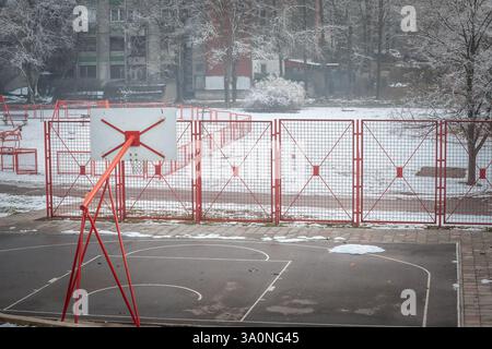 Un tabellone rosso da basket si trova in un campo urbano coperto di neve a Belgrado, in Serbia. Il freddo invernale contrasta con l'ambientazione del parco giochi, come illustrato Foto Stock