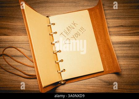 Una nota di ringraziamento su un notebook in pelle, su uno sfondo di legno Foto Stock
