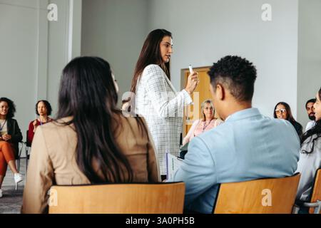 Donna d'affari che gestisce e parla durante una presentazione a un gruppo di colleghi diversi in un ambiente di ufficio moderno. Foto Stock